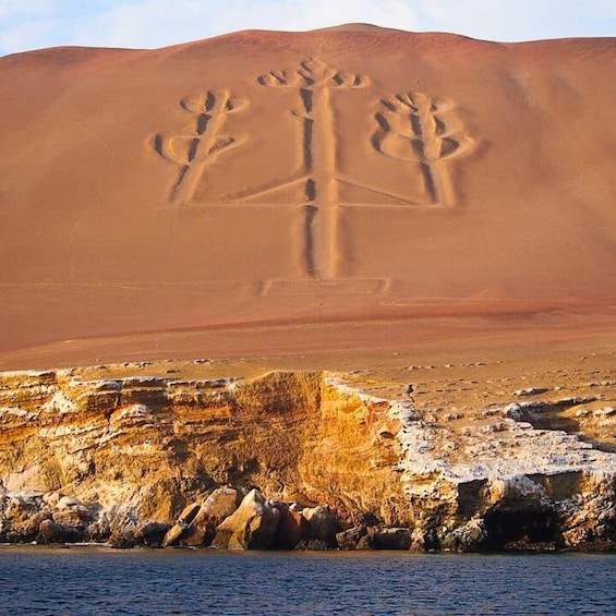 A desert landscape with a large sand dune and a rock formation with carved figures. 4