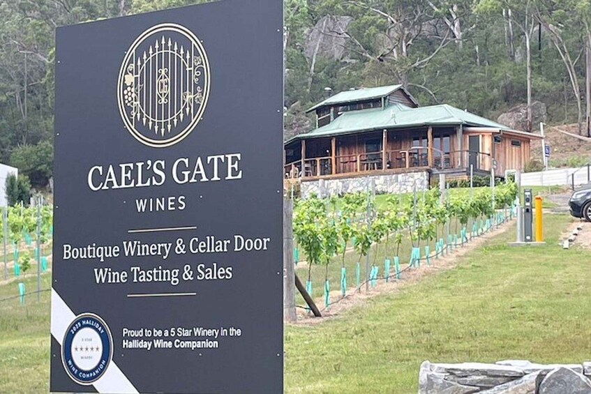 A sign for Cael's Gate Wines, a boutique winery and cellar door, with a view of the winery building and vineyard in the background. 5