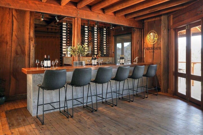 A rustic bar with wooden beams, a stone counter, and black bar stools. 3