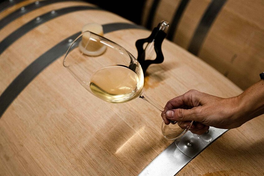 A hand holding a wine glass over a wooden barrel. 2