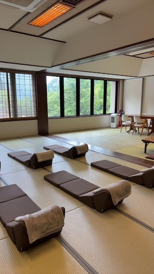 A tatami mat room with tatami mats, cushions, a projector screen, and a table with chairs. 3
