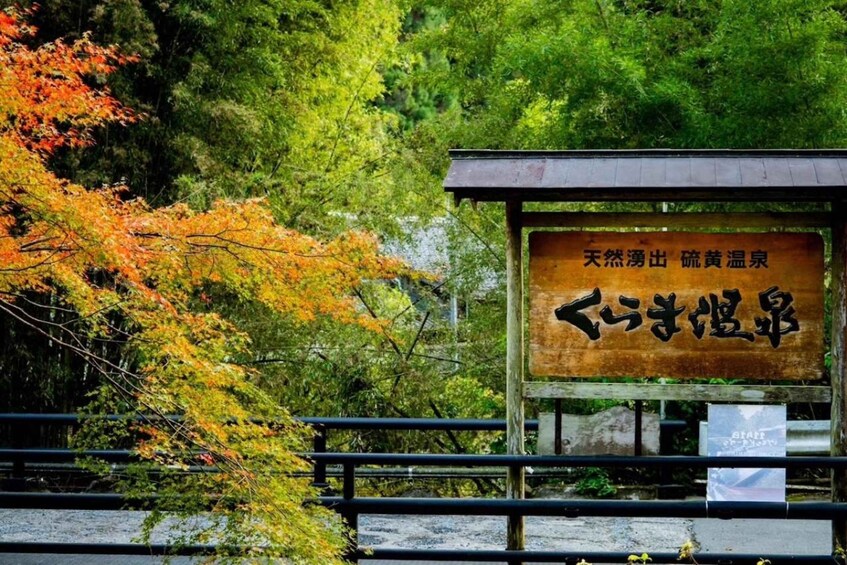 A wooden sign with Japanese characters, surrounded by autumn foliage and a metal railing. 2