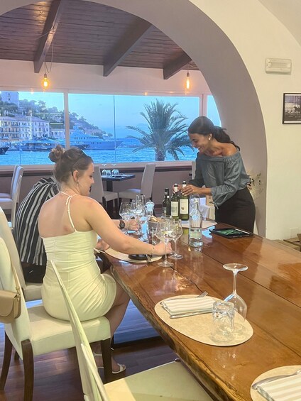 A woman at a bar with a view of the sea and buildings. 2