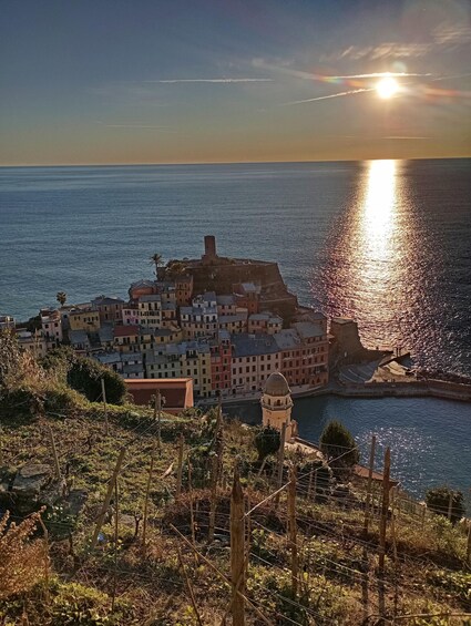 A coastal town with colorful buildings, a prominent tower, and a body of water reflecting the sun. 3
