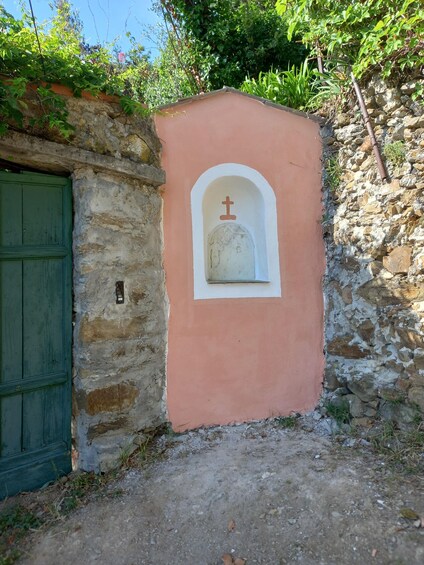 A rustic stone wall with a green door and a pink wall with a white arched window and a cross symbol. 2