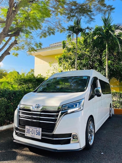 A white Toyota Innova parked in a lush green area with trees and a building in the background. 4
