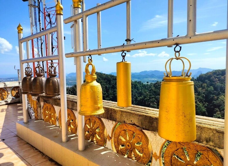A row of golden bells hanging from a railing with a scenic view of mountains in the background. 3