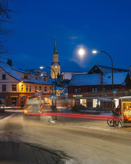 A snowy street at night with a church tower, streetlights, and a Coca-Cola bus stop. 3