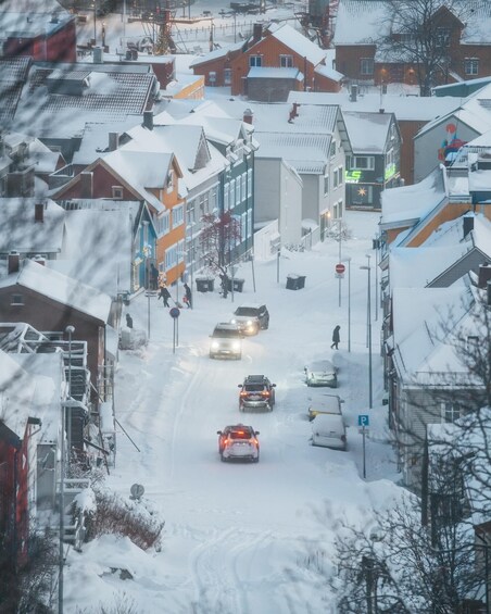 A snowy street lined with buildings, cars, and a pedestrian crossing. 5
