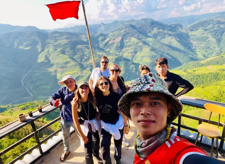 A group of people on a scenic overlook with a red flag, lush green hills, and a clear sky in the background. 3