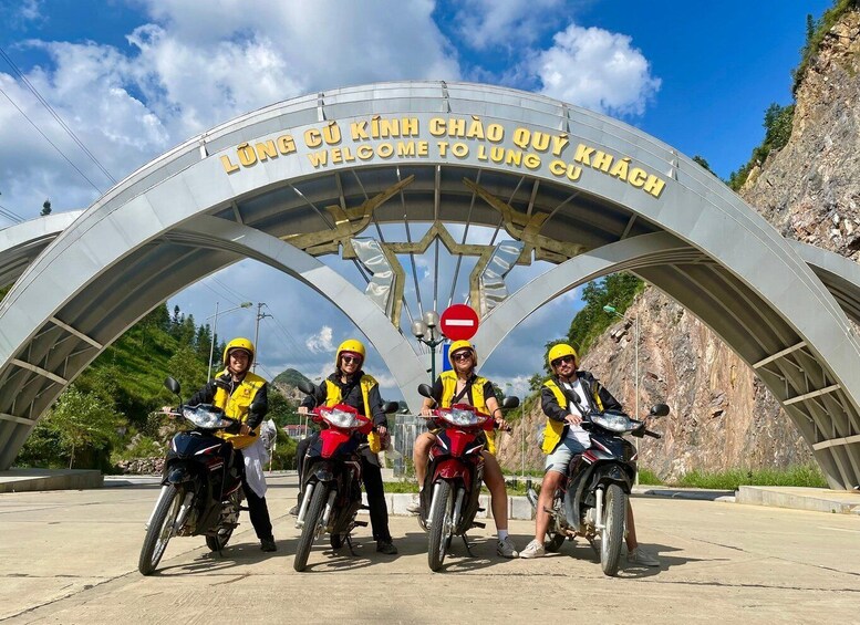 A group of motorcyclists at a tunnel entrance with a sign reading 'WELCOME TO LUNG CU.' 2