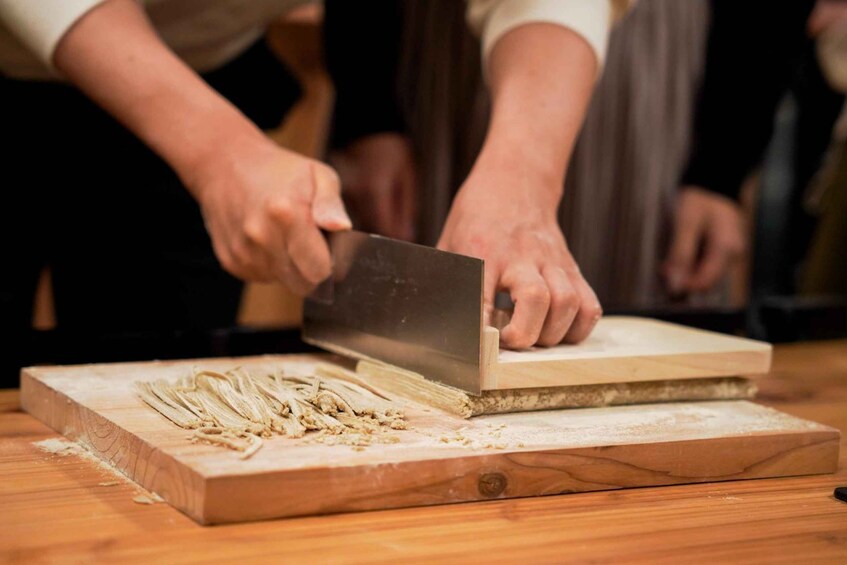 A person using a large knife to shave wood on a cutting block. 1