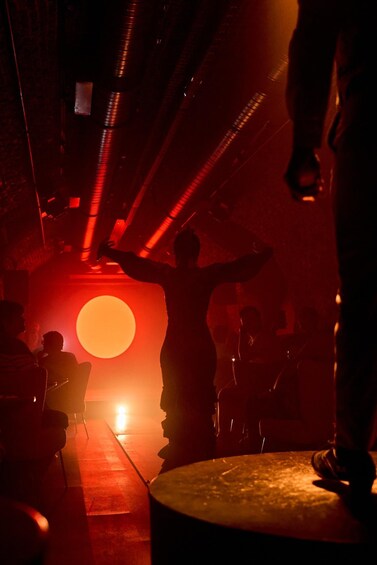 A dimly lit room with a large red light and silhouettes of people. 5