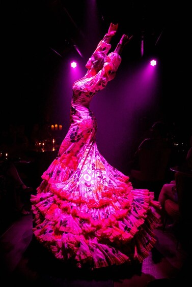 A person in a voluminous, floral-patterned dress with a dramatic, spiraling design, illuminated by stage lighting. 4