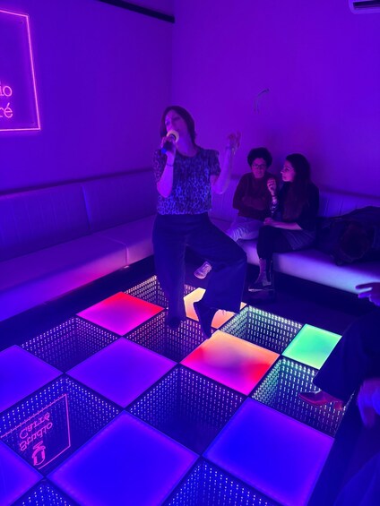 A person singing on a stage with a neon sign in the background. 5