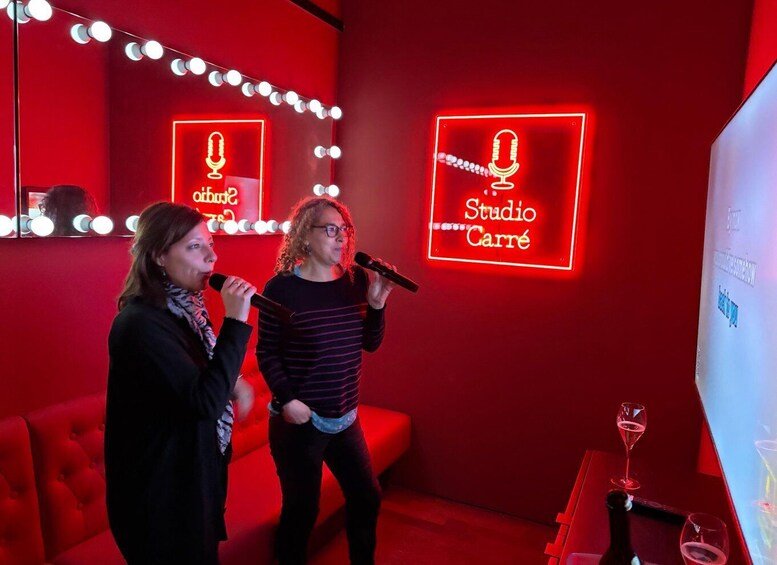 Two people singing in a red-lit room with neon signs reading 'Studio Carré.' 4