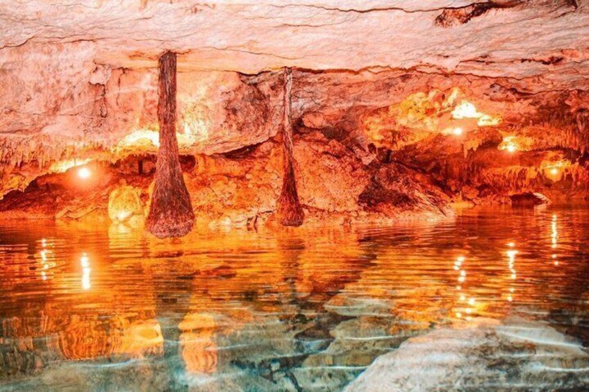 A cave with stalactites hanging from the ceiling and a reflective water surface below. 5