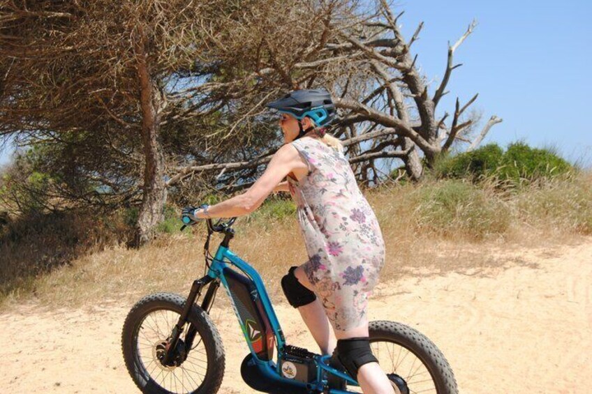 A person riding a blue electric bike on a sandy trail with trees in the background. 5