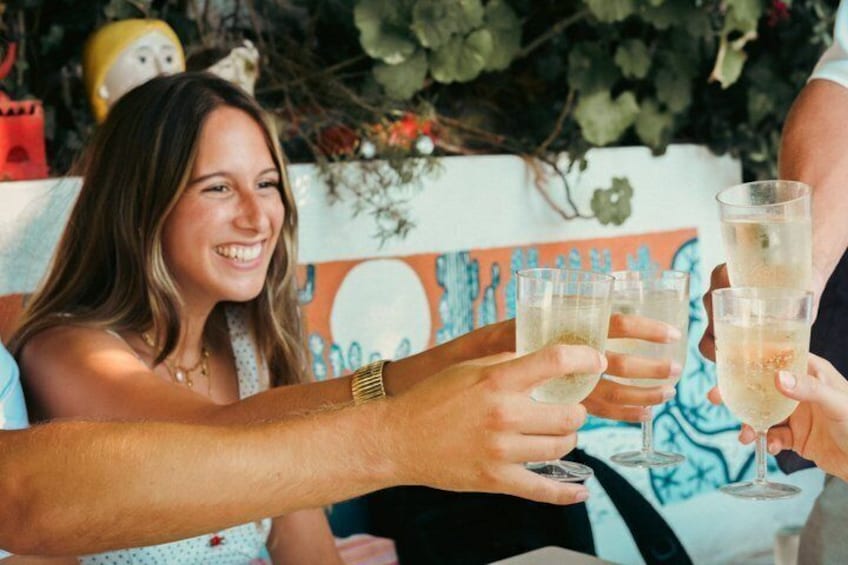 A person holding a glass of drink, with a colorful wall and greenery in the background. 1