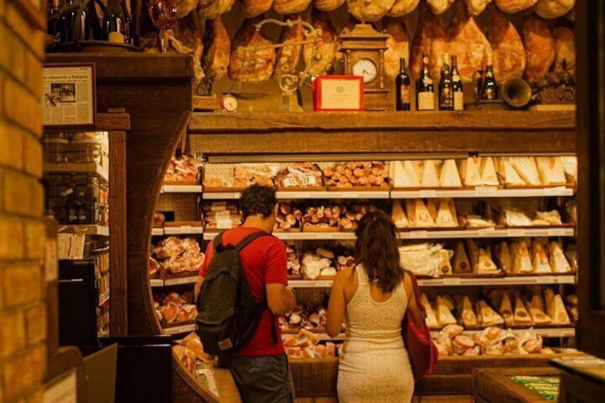 A person in a red shirt and a woman in a white dress browsing through a deli counter with various meats and cheeses. 3