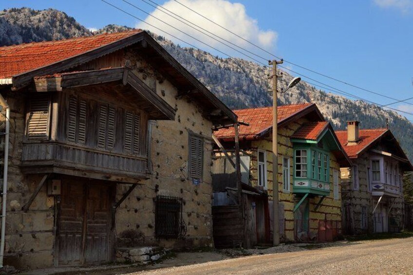 A row of rustic buildings with wooden balconies and red-tiled roofs, set against a mountainous backdrop. 5