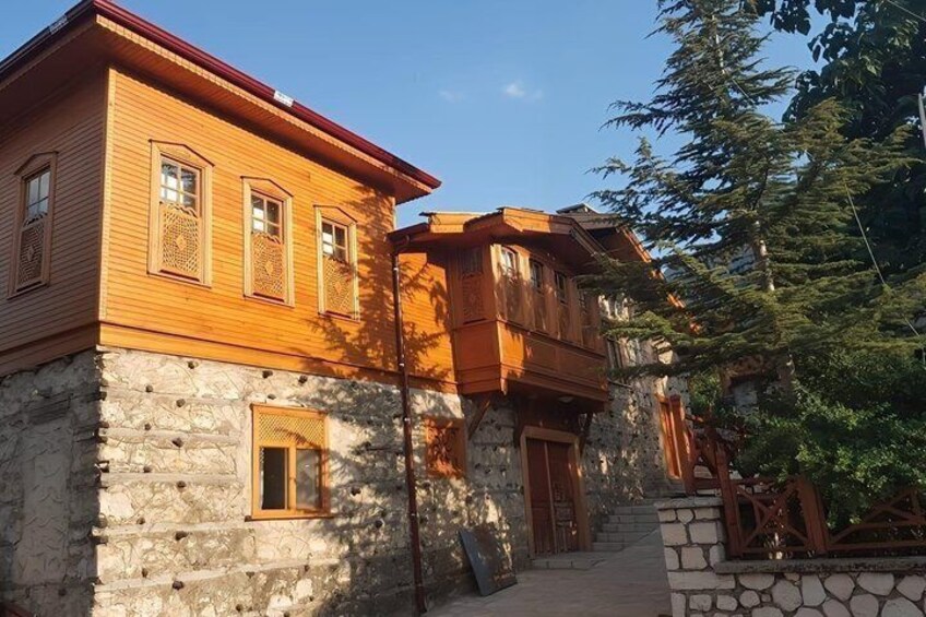 A two-story wooden house with stone foundation, wooden balcony, and a stone staircase. 4