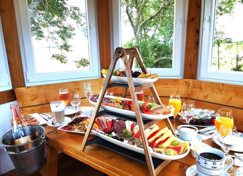 A wooden bench with a tiered fruit and cheese board, a bottle of champagne, and various breakfast items. 3