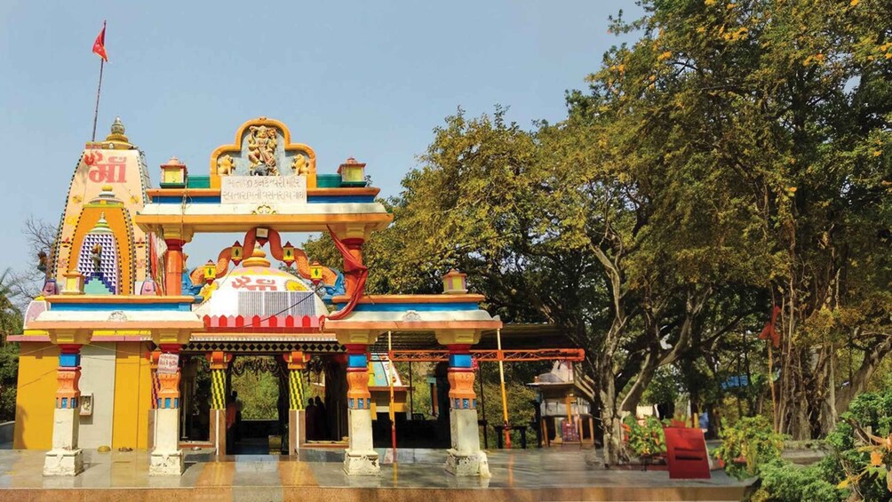 A colorful temple entrance with a flag, surrounded by trees. 1
