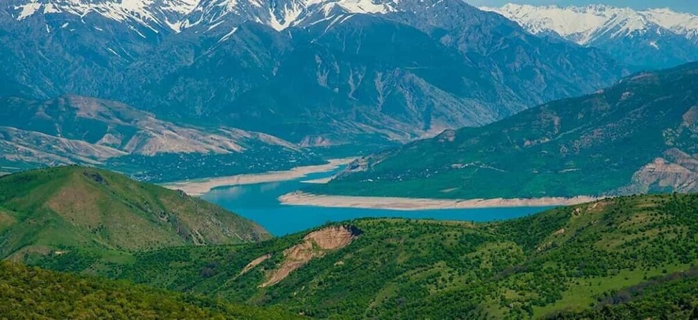 A mountainous landscape with a lake surrounded by green hills and snow-capped peaks. 1
