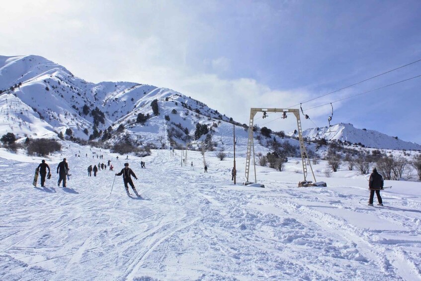 A snowy ski slope with skiers, a ski lift, and mountains in the background. 4