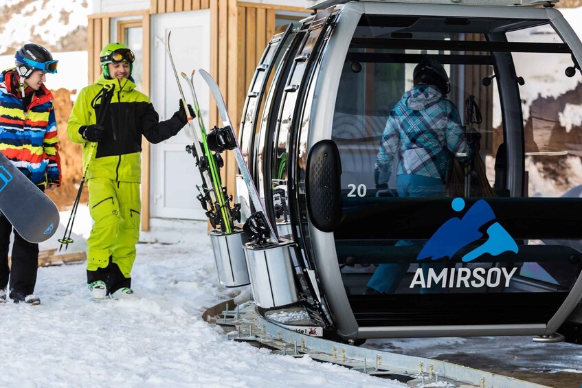 A ski lift with skiers and a snowboarder, and a vehicle with the AMIRSOY logo. 3