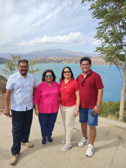 Four people standing on a concrete ledge with a lake and mountains in the background. 2