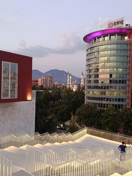 A modern building with a 'tring' sign, a mosque with minarets, and a mountain in the background. 4