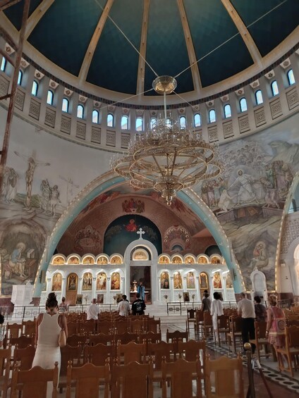 An interior of a church with a large chandelier, arched ceilings, and religious murals. 3