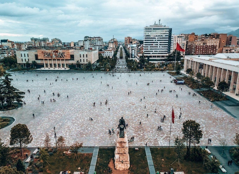 A plaza with a large open space, a statue, and surrounding buildings. 1