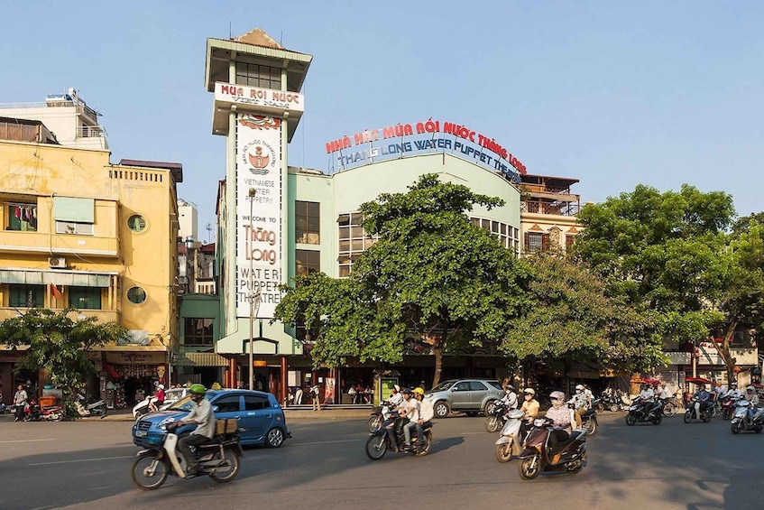 A busy street with motorcycles, a water puppet theater, and various buildings. 3