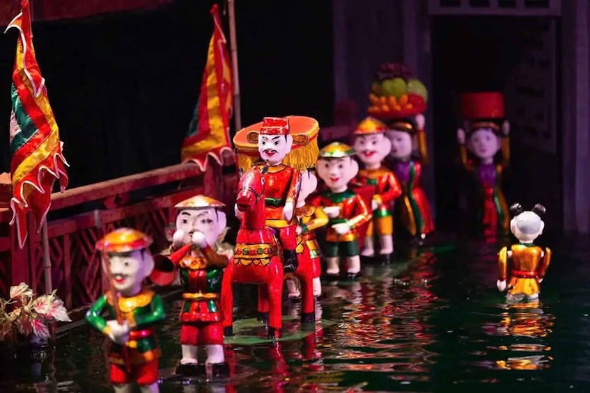 A group of performers in traditional costumes on a stage with a water feature. 1