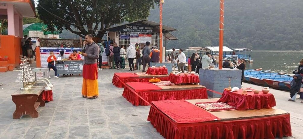 A riverside event with tables set up for a ceremony, people gathered around, and a ticket counter in the background. 5