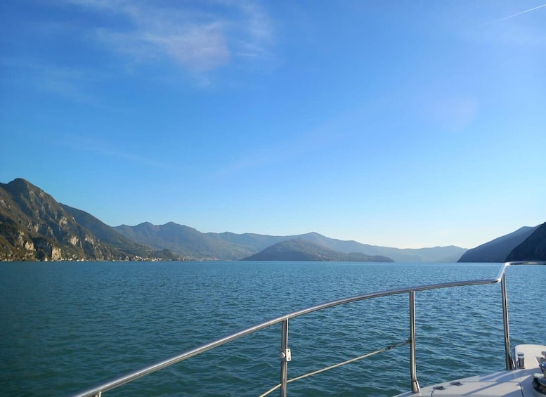 A calm lake with mountains in the background and a boat's railing in the foreground. 2