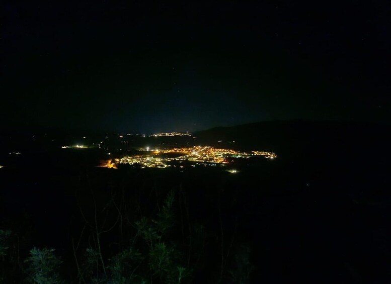 A nighttime view of a city with a dense cluster of lights, surrounded by hills. 1