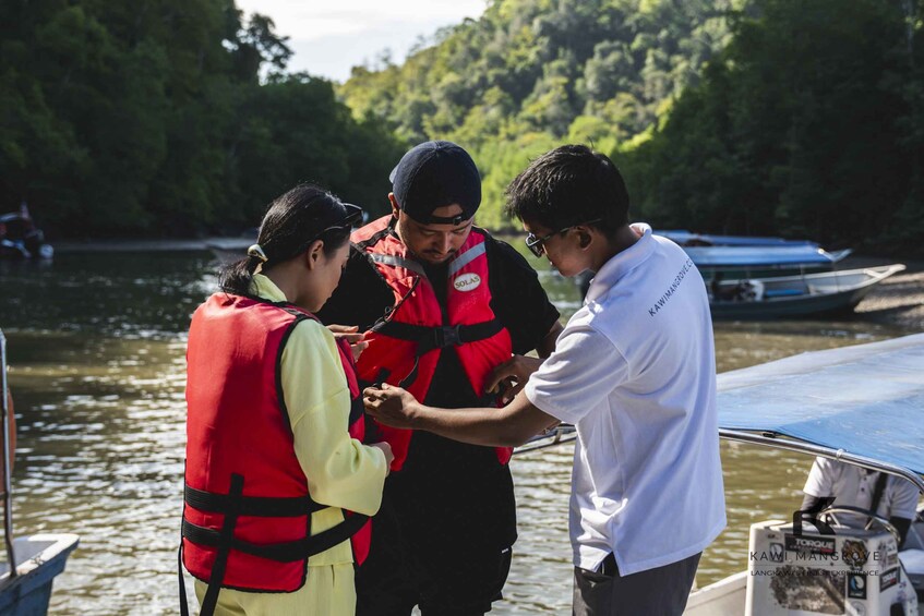 People on a boat wearing life jackets, with a forested riverbank in the background. 2