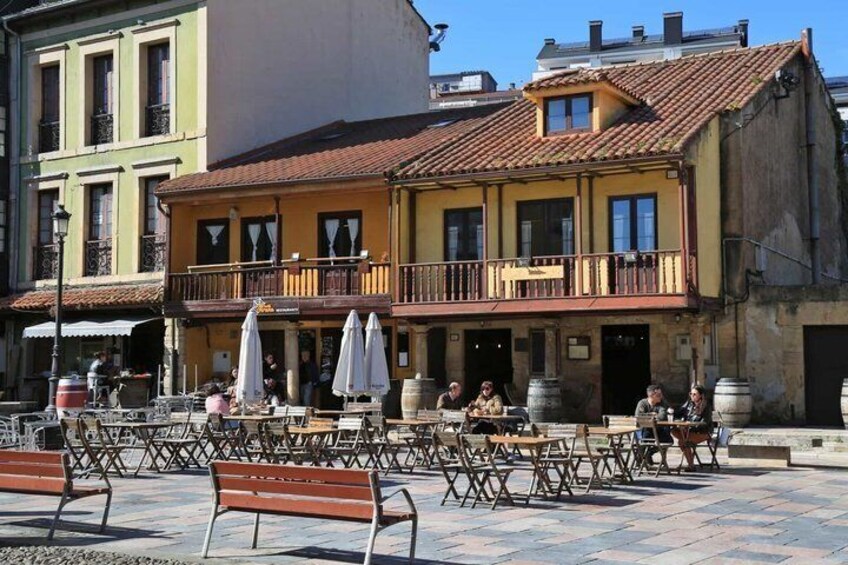 A courtyard with outdoor seating, a yellow building with a balcony, and a green building in the background. 4