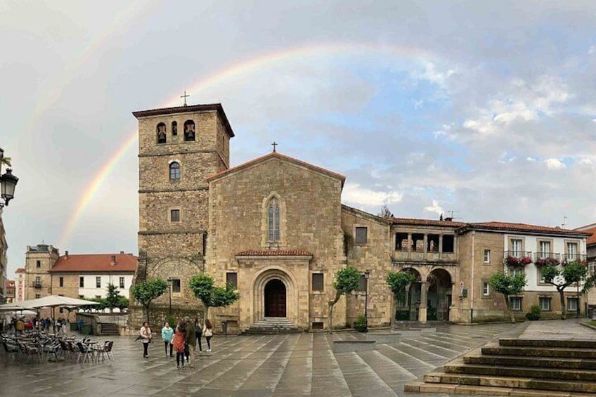 A historic church with a bell tower, a cobblestone square, and a rainbow in the sky. 2
