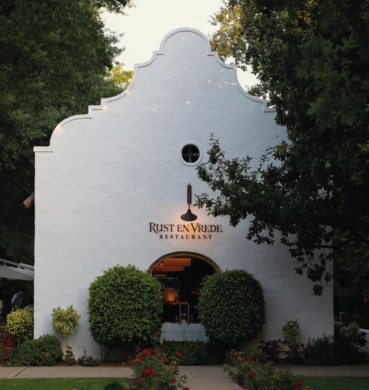 A white building with a rounded top and a small circular window, labeled 'Rust En Vrede Restaurant.' 4