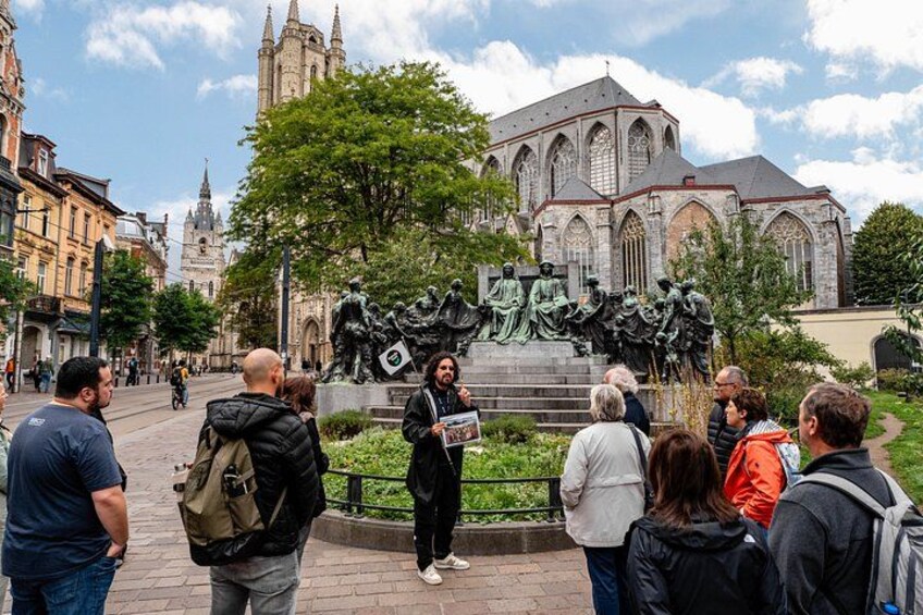 A group of people gathered around a statue in a city square with a cathedral in the background. 4