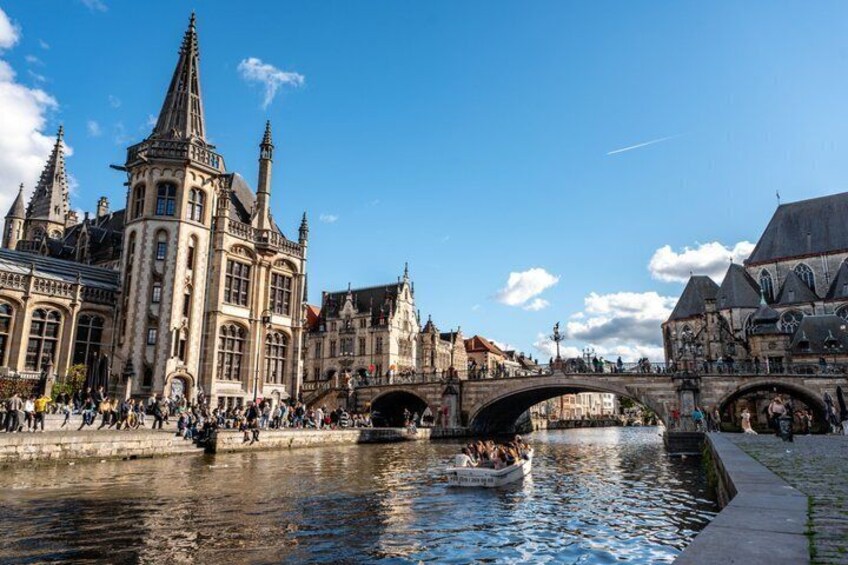 A historic building with pointed towers, a river with a boat, and a bridge connecting two parts of the city. 1
