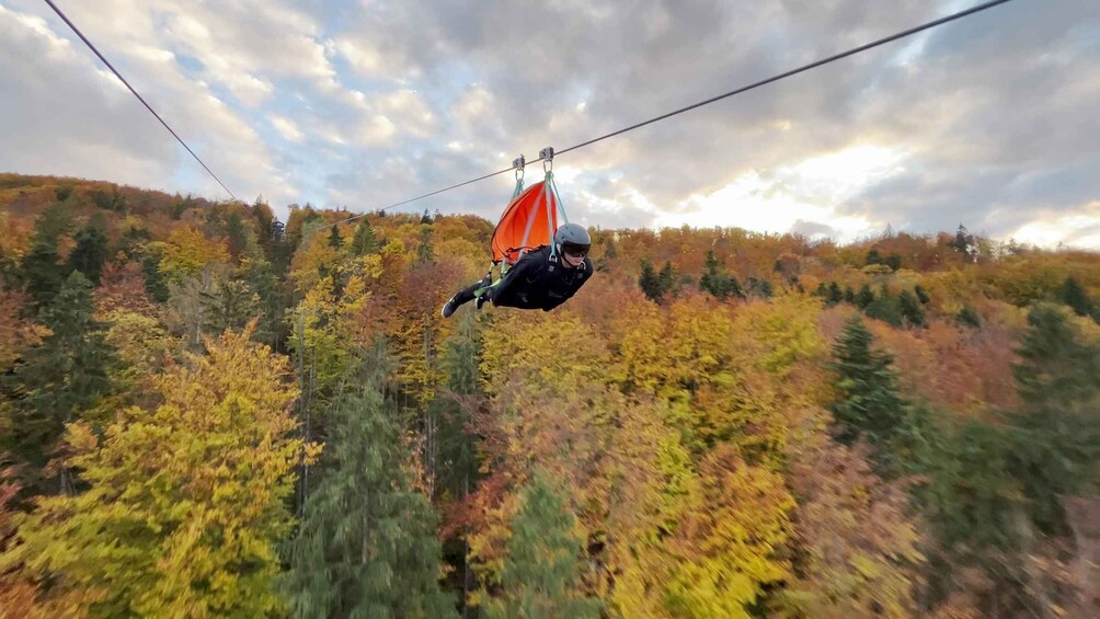 A person skydiving with an orange parachute over a forested landscape. 3