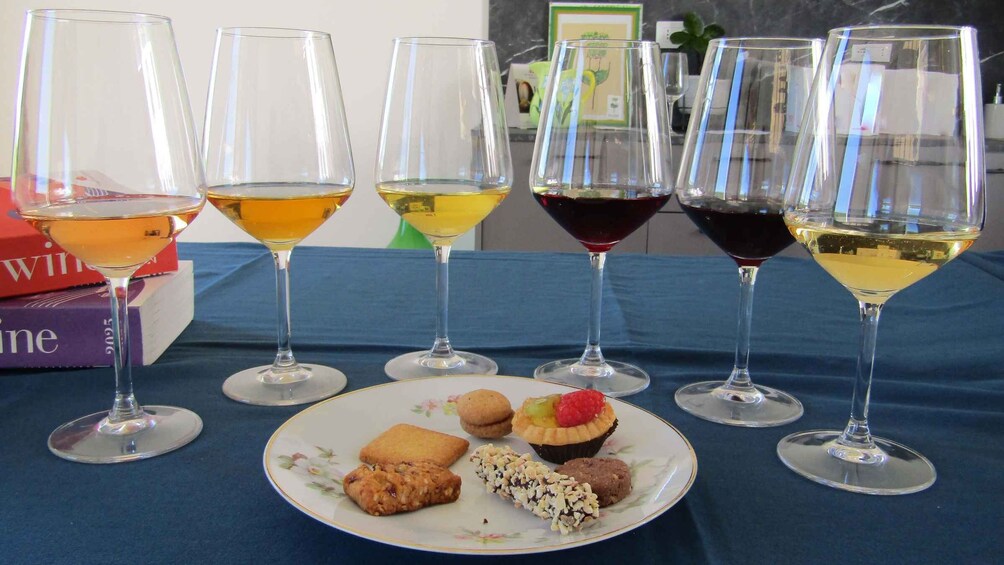 A table with six wine glasses, a plate with pastries, and books. 1