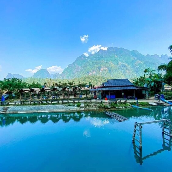 A clear swimming pool with a wooden deck, a pavilion, and a mountain backdrop. 2