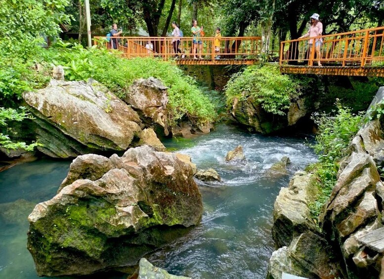 A river flowing through a rocky landscape with a wooden bridge and people walking across it. 4